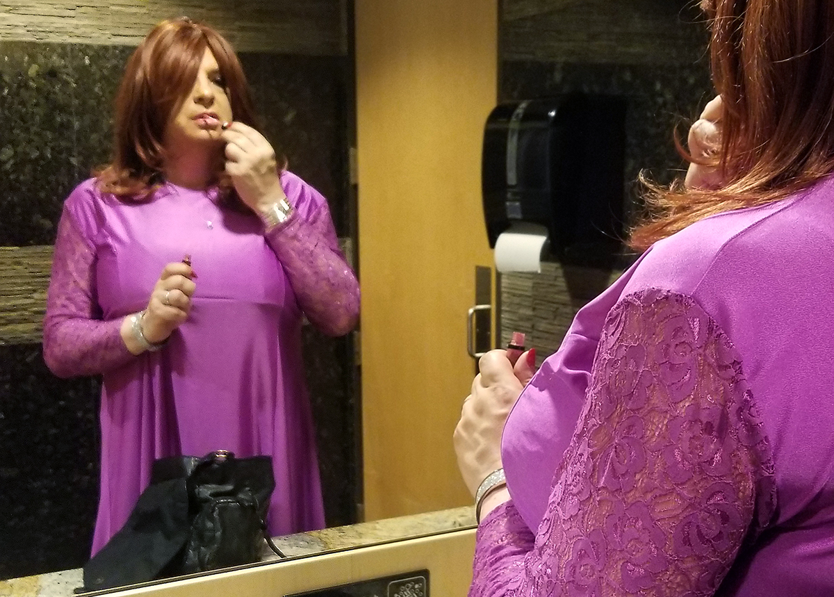 Sissy josephine applies lip gloss in the Women's restroom.